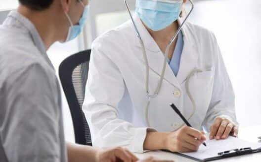 마스크를 쓴 의료진이 진료실에서 환자와 마주 앉아 상담 내용을 기록하는 모습으로, 붓기가 잘 빠지지 않을 때 의료 상담이 필요한 상황을 표현한 이미지.