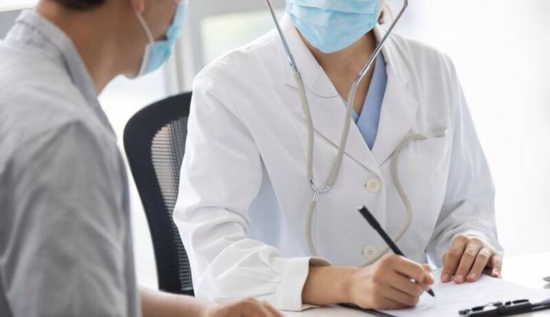 마스크를 쓴 의료진이 진료실에서 환자와 마주 앉아 상담 내용을 기록하는 모습으로, 붓기가 잘 빠지지 않을 때 의료 상담이 필요한 상황을 표현한 이미지.