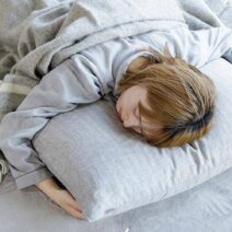 침대 위에서 엎드려 베개를 안고 깊이 잠든 모습으로, 엎드려 잘 때 얼굴이 압박되며 붓기가 심해질 수 있는 상황을 보여주는 이미지.