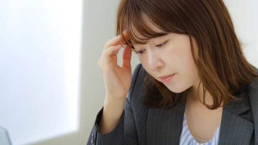 피로한 표정으로 목 부근을 신경 쓰는 듯한 여성이 고민하는 모습으로, 호르몬 변화나 갑상선 이상으로 인해 나타날 수 있는 붓기 증상을 설명할 때 사용하는 이미지.