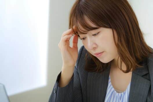 피로한 표정으로 목 부근을 신경 쓰는 듯한 여성이 고민하는 모습으로, 호르몬 변화나 갑상선 이상으로 인해 나타날 수 있는 붓기 증상을 설명할 때 사용하는 이미지.