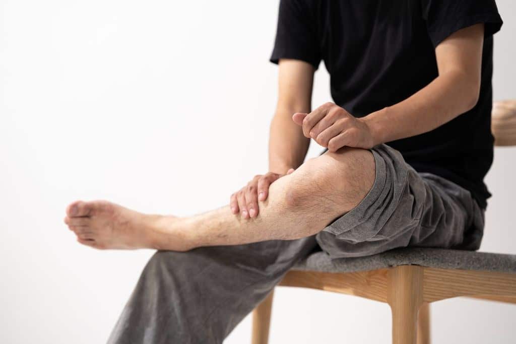 의자에 앉아 다리와 무릎 부위를 만지고 있는 모습으로, 몸이 자꾸 붓고 하체에 불편감이 느껴지는 상황을 표현한 이미지.