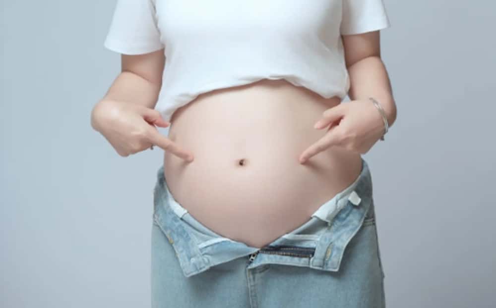 임신으로 인해 아랫배가 팽팽해진 상태를 손으로 가리키는 모습으로, 임신 중 붓기와 체형 변화를 설명할 때 사용하는 이미지.